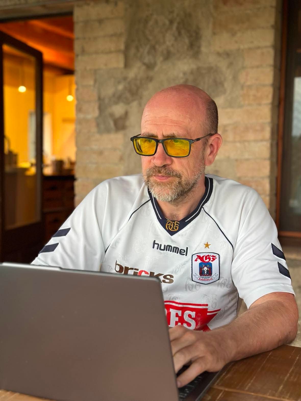 Laust Kehlet sidder ved sin bærbare computer i hvid AGF-trøje under en overdækket terrasse